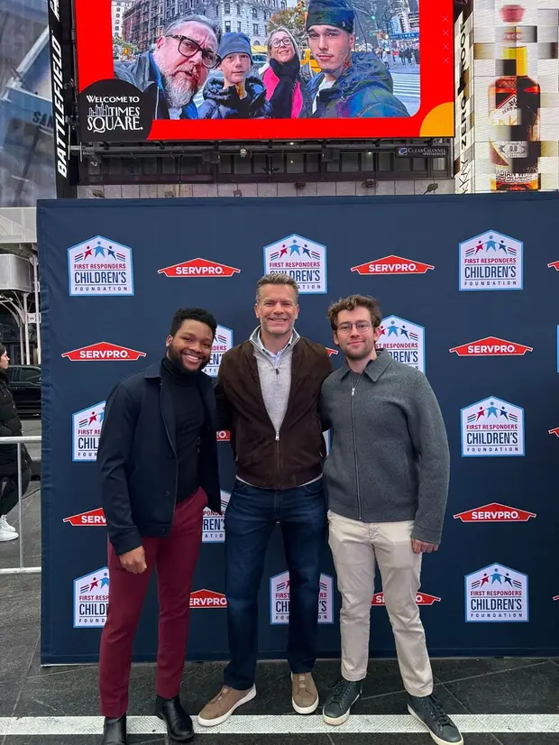 Founders Dory Aine and Josh Cohn with Rob Allen in front of a SERVPRO and First Responders Children's Foundation banner in Times Square